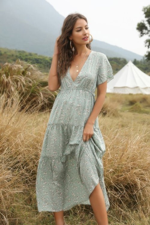 Woman in a green dress standing in a field with mountains in the background