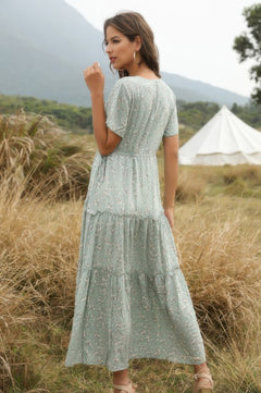 Woman in a light green dress standing in a field with a tent and mountains in the background