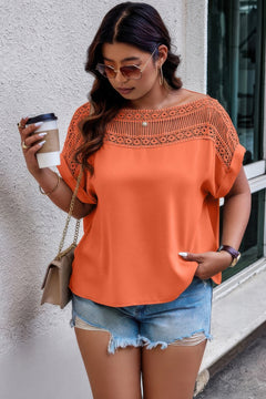 Woman wearing an orange top with lace details and denim shorts, holding a coffee cup.