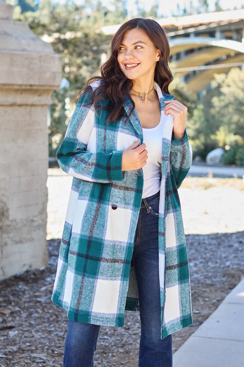 Woman wearing a plaid coat outdoors with trees and a building in the background
