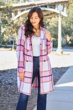 Woman wearing a pink plaid coat outdoors on a sunny day.