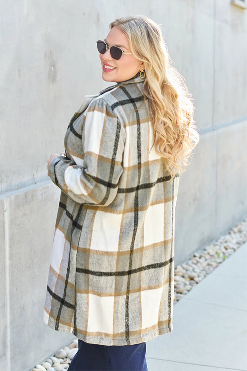 Woman wearing a plaid coat standing against a light-colored wall.