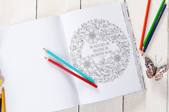 Coloring book with a floral design and text, surrounded by colored pencils on a wooden surface.