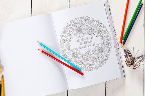 Coloring book with a floral design and text, surrounded by colored pencils on a wooden surface.