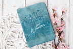 Blue pouch with 'Strength for Today for Women' text on a decorative white surface with flowers.