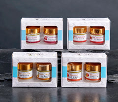 A 2-piece all-natural lip care gift set from The Grecian Soap Company featuring a small jar of lip scrub and a matching jar of lip balm with elegant gold lids, packaged in a white windowed gift box. Available in Raspberry, Strawberry, Mango, and Pina Colada.