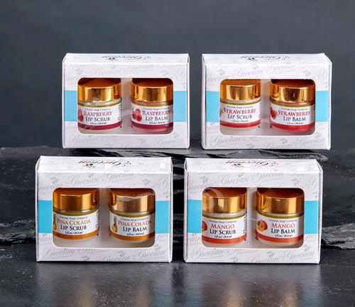 A 2-piece all-natural lip care gift set from The Grecian Soap Company featuring a small jar of lip scrub and a matching jar of lip balm with elegant gold lids, packaged in a white windowed gift box. Available in Raspberry, Strawberry, Mango, and Pina Colada.