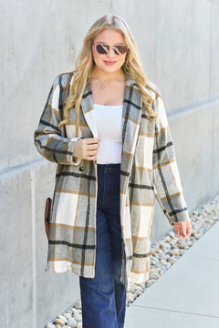 Woman wearing a plaid coat standing against a light-colored wall.