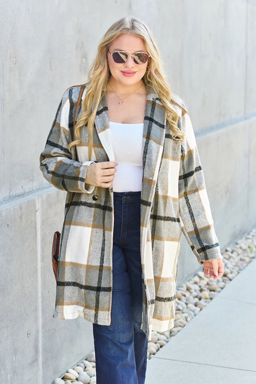 Woman wearing a plaid coat standing against a light-colored wall.