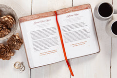 Open book with a red ribbon on a wooden surface with coffee cups and decorative items.