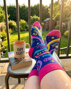 Colorful socks with text worn by a person sitting on a railing with a mug and book.