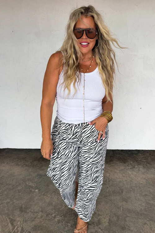 Woman styling zebra print barrel jeans with a white tank top and accessories.