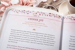 Open book with inspirational text on a table with flowers and a cup of coffee.