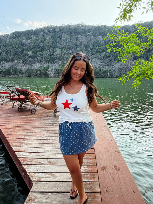 Woman wearing a white ribbed, stretchy tank top featuring printed star patches in red and blue.