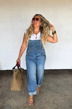 Model walking in Blakeley Coast barrel leg denim overalls featuring a front bib pocket and adjustable straps.