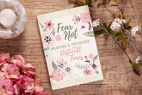 Book titled 'Fear Not: Prayers & Promises for Difficult Times' on a wooden surface with flowers and a candle.