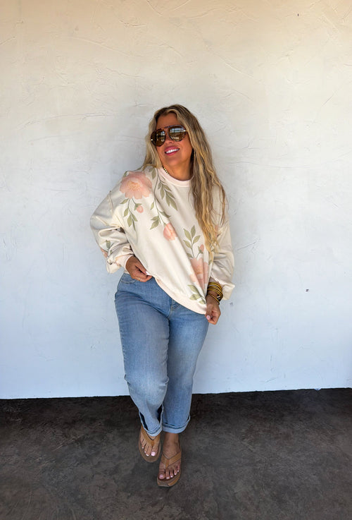 Woman wearing a white floral top and blue jeans against a white wall.