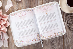 Open book with floral design on a wooden surface with coffee and flowers.