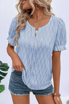 Woman wearing a textured notched short sleeve blouse in cerulean, styled with layered necklaces and denim shorts. Perfect spring or summer top for women.
