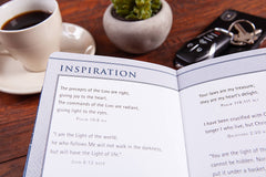Open book with inspirational text for a graduate on a wooden table with a cup of coffee, plant, and keys.