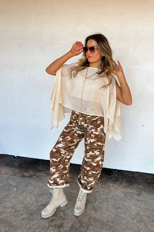 Woman wearing a beige outfit with camouflage pants against a white wall.