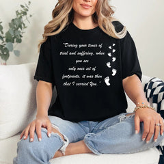 Person wearing a black t-shirt with a motivational quote and footprints graphic, sitting on a couch.