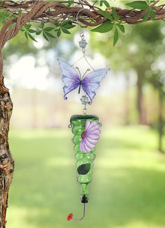 A hanging 28-inch green glass hummingbird feeder with a decorative metal purple butterfly and flower accent in a garden setting.