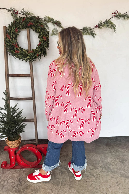 Person wearing a pink cardigan with candy cane pattern in a festive setting.