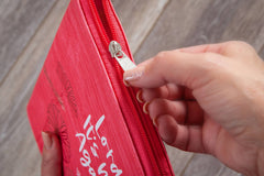 Red zippered pouch with white text on a wooden surface