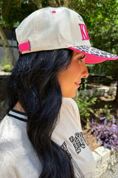 Woman wearing a beige cap with pink brim and leopard print bill, standing outdoors.