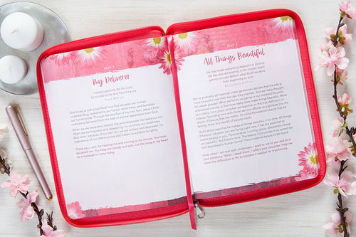 Open book with floral design on a white surface with candles and flowers.