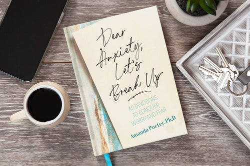 Hardcover book 'Dear Anxiety, Let’s Break Up' by Amanda Porter Ph.D on a wooden desk with a cup of coffee.
