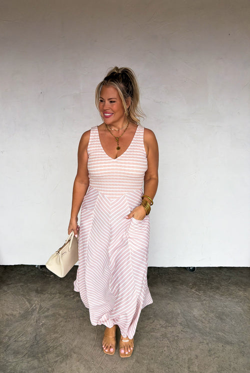 Woman wearing a pink striped dress against a white wall.