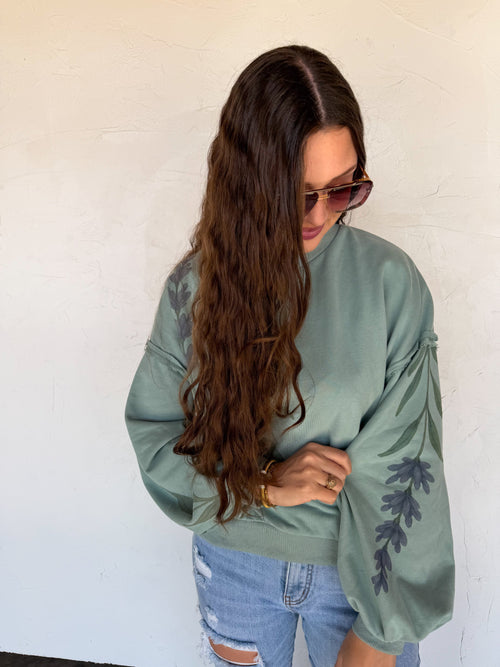 Woman wearing a light green sweater with floral patterns against a white wall