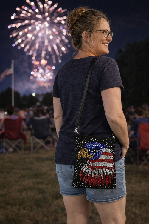 Woman outdoors at a park wearing a black rhinestone eagle crossbody bag while watching fireworks