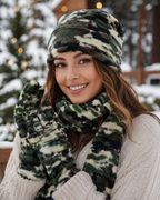 A smiling woman outdoors in a snowy setting wearing a matching camouflage fleece beanie, scarf, and knit mittens.