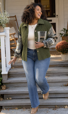A woman walking down wooden steps outdoors wearing a green corduroy button-front jacket with patterned knit sleeves, a cream top, blue jeans, and tan boots.