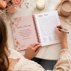 Person writing in a spiral-bound notebook with a candle and flowers in the background