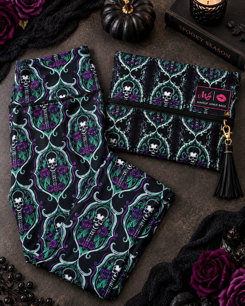 A gothic-themed two-piece set featuring a matching pair of leggings and a zippered pouch. The fabric has a black background with a repeating pattern of purple roses, green leaves, and white skulls framed by teal baroque scrolls.