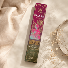 A boxed incense stick package labeled Buddha Blessing and Magical Forces, photographed on a warm cream surface with draped fabric, dried flowers, and a ceramic plate nearby.
