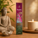 A box of Buddha Blessing Magical Sparkle Incense Sticks stands on a wooden surface between a seated Buddha statue and a lit candle, with warm ambient lighting and soft background decor.