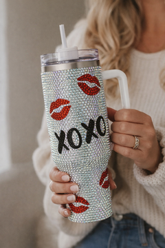 Person holding a blinged-out tumbler with 'XOXO' and lip prints.