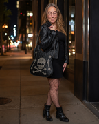 Woman in black outfit with skull-patterned bag on a city street at night