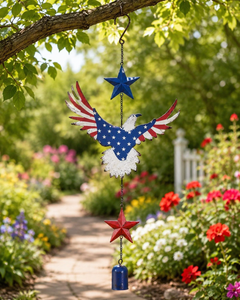 Americana eagle garden hanging chime hanging from a tree branch above a colorful flower garden path.
