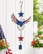 Red white and blue eagle hanging chime displayed against a white porch wall with flowers and an American flag accent.