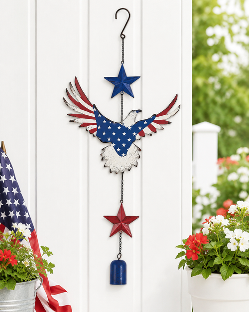 Red white and blue eagle hanging chime displayed against a white porch wall with flowers and an American flag accent.