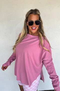 Woman wearing oversized mauvy pink athleisure sweatshirt with thumbholes and high/low hem.