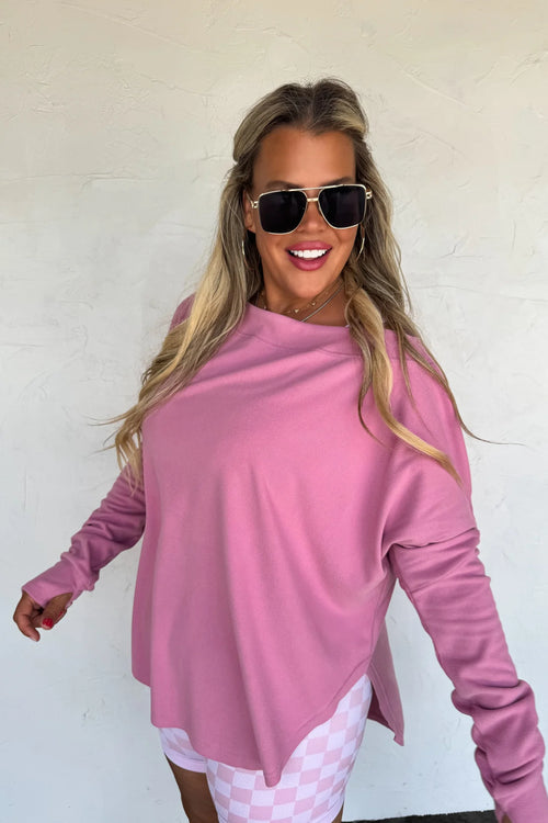 Woman wearing oversized mauvy pink athleisure sweatshirt with thumbholes and high/low hem.