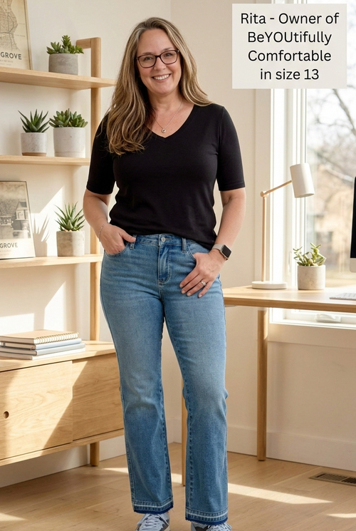 Woman wearing a black shirt and blue jeans standing in a bright room with wooden furniture and plants.