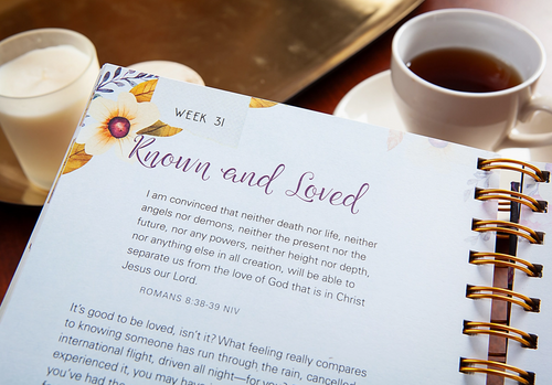 Open planner with a quote on a table with a cup of coffee and a glass of milk.